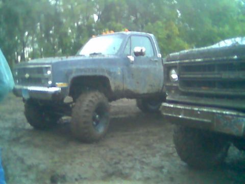 1976 GMC C/K Pickup - Two mud-covered pickup trucks are parked in a muddy outdoor area.