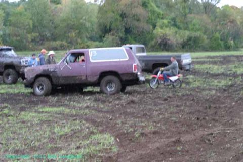 1976 GMC C/K Pickup - Several vehicles are in a muddy field, with a person riding a dirt bike near a purple SUV.