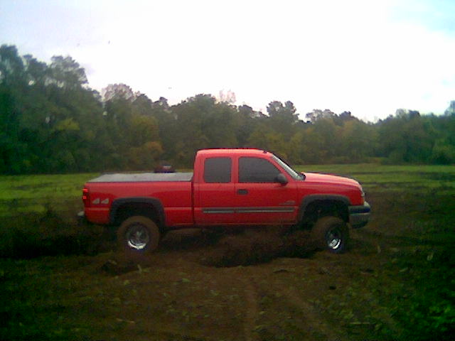 Red pickup truck with a bed cover driving through mud with trees in the background