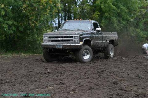 1976 GMC C/K Pickup - A black pickup truck navigates a muddy terrain, kicking up dirt as it moves.