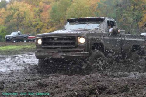 1976 GMC C/K Pickup - A GMC C/K Pickup truck navigates a challenging mud bog, with another truck visible in the background.