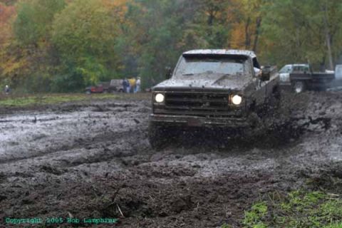 1976 GMC C/K Pickup - A muddy pickup truck navigates a challenging off-road course with other vehicles in the background.