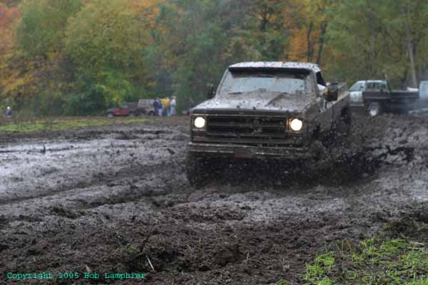 Mud-splattered pickup truck driving through mud, front view. Visible grille and headlights