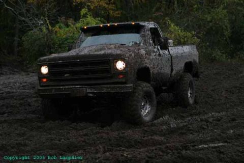 1976 GMC C/K Pickup - This heavily mud-covered pickup truck navigates a muddy terrain, its front end prominently displayed.