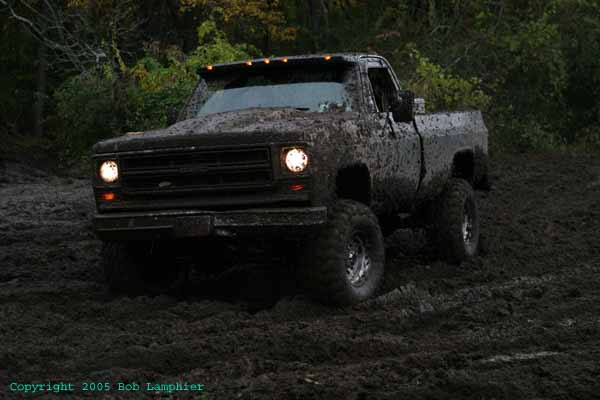 Mud-covered pickup truck driving through mud, front view