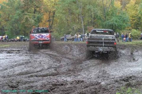1976 GMC C/K Pickup - Trucks churn through deep mud during an off-road event, with spectators gathered in the background.