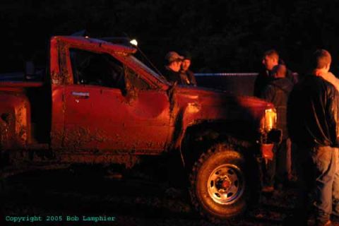 1976 GMC C/K Pickup - A red pickup truck is heavily covered in mud, seen from the driver's side at night.