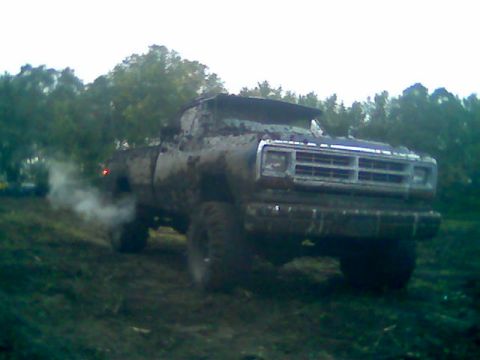 1976 GMC C/K Pickup - This heavily soiled pickup truck appears to be from the 1970s, possibly a Dodge Ram, navigating a muddy terrain.