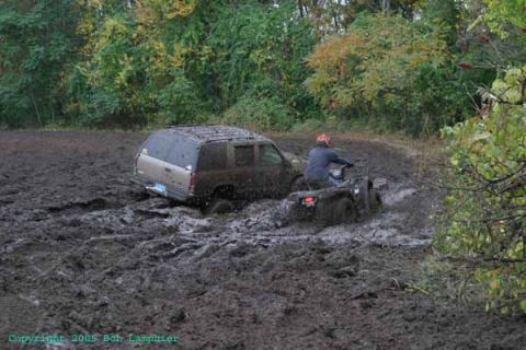 1976 GMC C/K Pickup - An SUV and an ATV are stuck in deep mud, surrounded by trees.