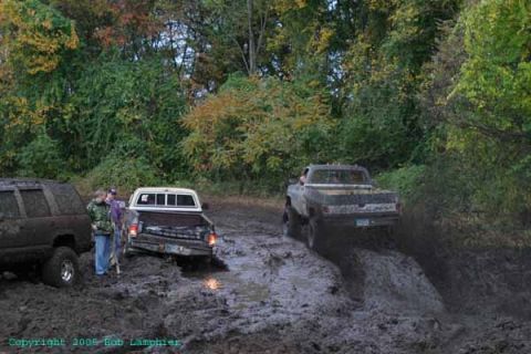 1976 GMC C/K Pickup - Off-road trucks navigate a challenging muddy terrain during an outdoor excursion.