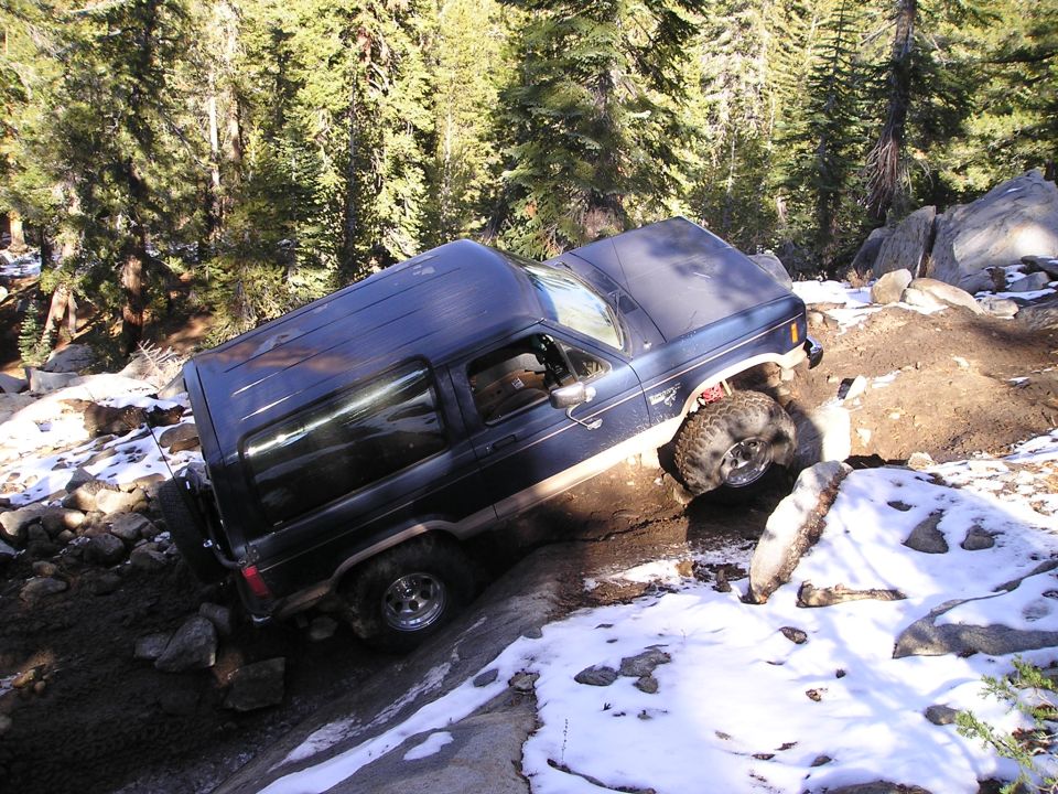 Dark blue SUV with a spare tire on the back, tilted on a rocky, snowy trail