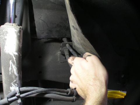 2000 Ford Excursion - Close-up of a hand manipulating brake lines and hoses on the underside of a vehicle.