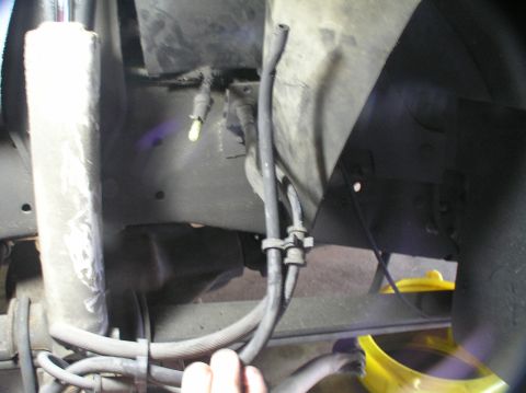 2000 Ford Excursion - Close-up view of the undercarriage, showing brake lines and a shock absorber, with a yellow pan positioned to catch fluid.