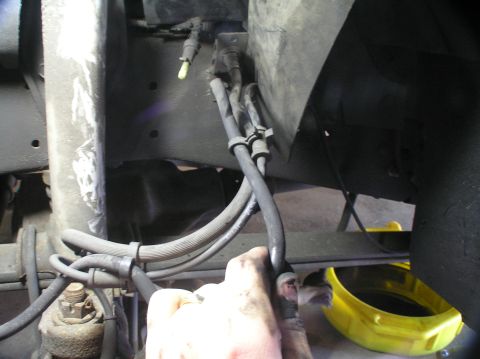 2000 Ford Excursion - Mechanic's hand working on brake lines near the suspension system, with a drain pan visible.