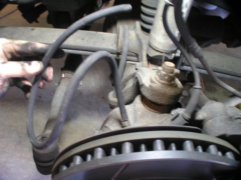 2000 Ford Excursion - Close-up view of vehicle suspension and brake components, with a hand holding a hose.