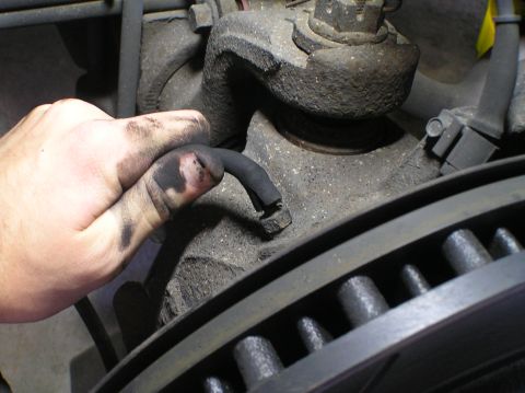 2000 Ford Excursion - A hand holds a broken vacuum line, indicating a potential issue with the vehicle's vacuum system near the brake assembly.