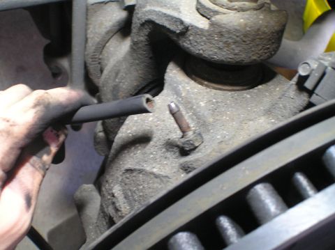 2000 Ford Excursion - A mechanic's hand holds braided lines near a vehicle's suspension components.