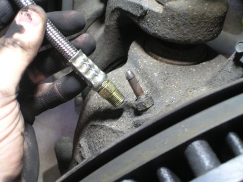 2000 Ford Excursion - Braided brake line being connected to a bleeder valve on a vehicle's brake assembly.