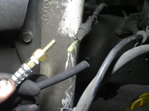 2000 Ford Excursion - A brass vacuum line adapter is held near a damaged rubber hose, likely for a vehicle's vacuum system.