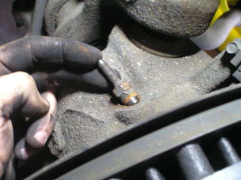 2000 Ford Excursion - A close-up shows a hand with grease on it, holding a brake bleeder valve near the brake rotor.