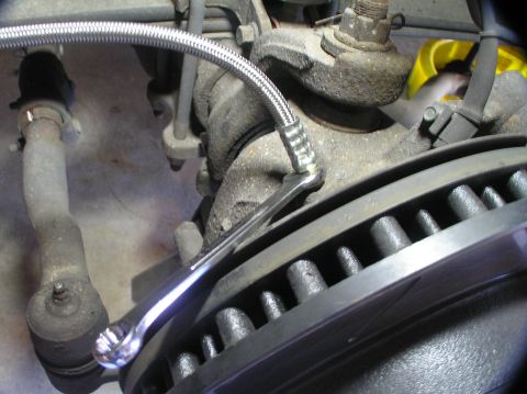 2000 Ford Excursion - A braided brake line is being tightened onto a caliper with a wrench, with a vented rotor visible in the foreground.