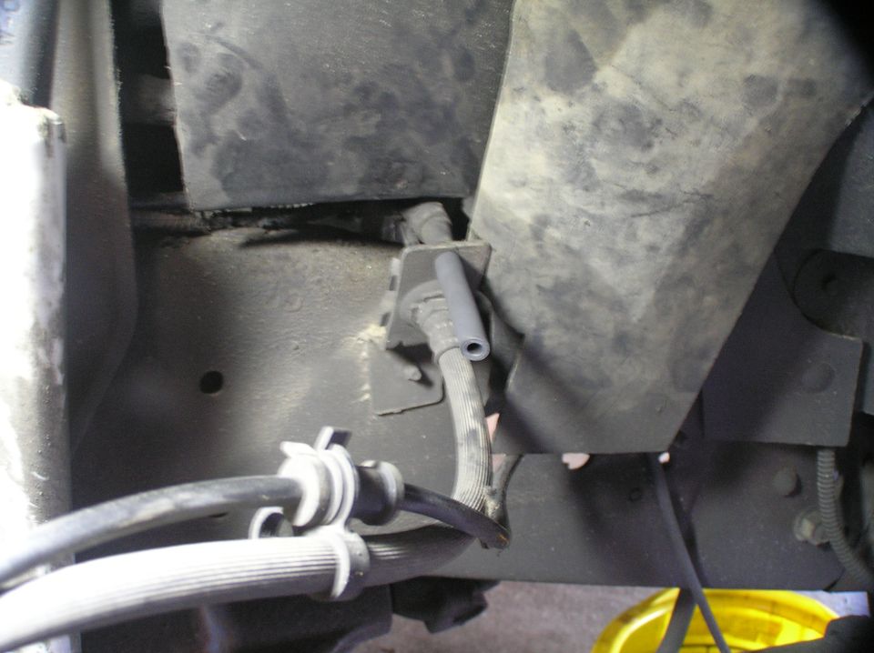 Undercarriage showing gray rubber hose, black bracket and clamped cables on vehicle frame