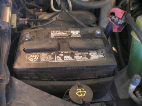 2000 Ford Excursion - Close-up of a vehicle's battery, showing various warning labels and a red terminal cover.