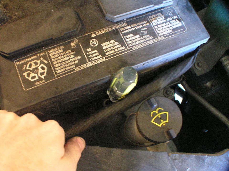 Car battery with warning label beside black washer fluid cap with yellow wiper icon