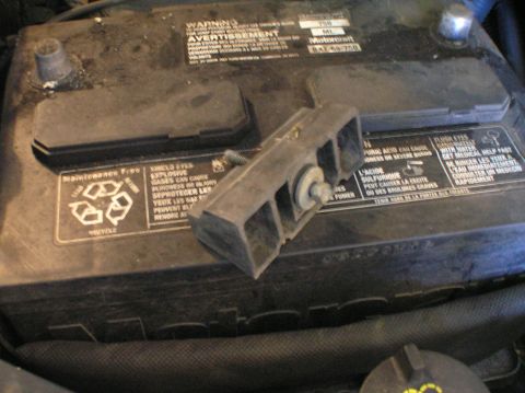 2000 Ford Excursion - A battery hold-down bracket is secured to a Motorcraft battery with a bolt and washer.