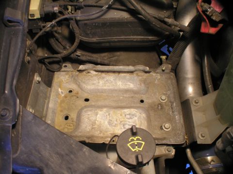 2000 Ford Excursion - Close-up of a vehicle's engine bay, focusing on the battery tray and a windshield washer fluid cap.