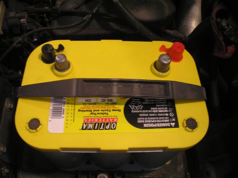 2000 Ford Excursion - Close-up of a yellow Optima battery with its terminals and warning labels visible.