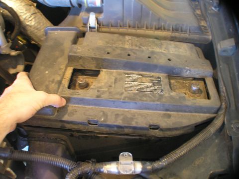 2000 Ford Excursion - A hand is shown lifting the cover of a vehicle's battery compartment, revealing the battery terminals.