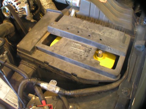 2000 Ford Excursion - Close-up of a car battery compartment showing a yellow Optima battery and its black cover.
