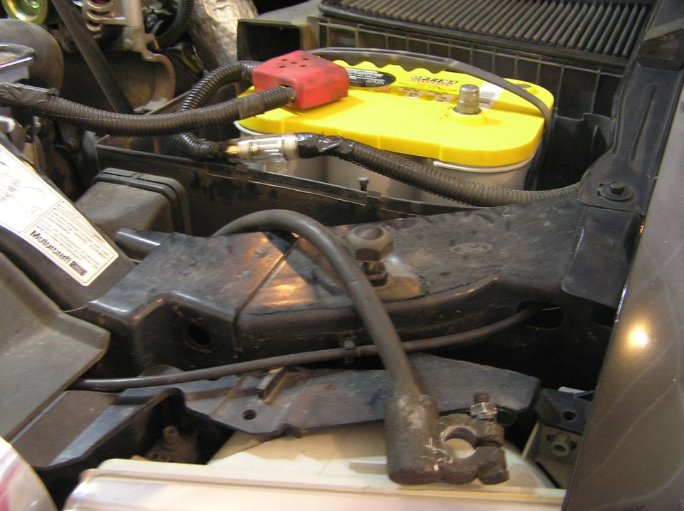 Engine bay with yellow-top battery, red terminal cover, and disconnected negative cable