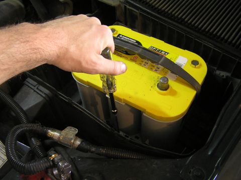2000 Ford Excursion - A hand uses a screwdriver on a yellow Optima battery in an engine bay.