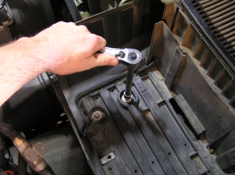 2000 Ford Excursion - Mechanic's hand operating a socket wrench on a bolt within a plastic housing.