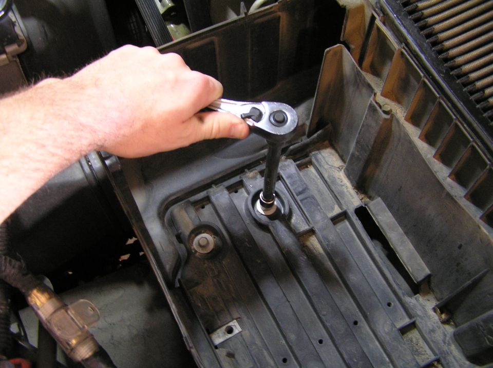 Hand using ratchet and extension in an empty black battery tray