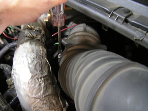 2000 Ford Excursion - Close-up of a hand working on a vehicle's engine intake system with a screwdriver and clamp.