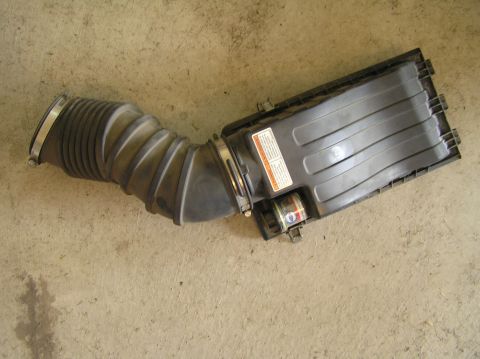 2000 Ford Excursion - A vehicle's air intake assembly, including a flexible hose and filter box, rests on a concrete surface.