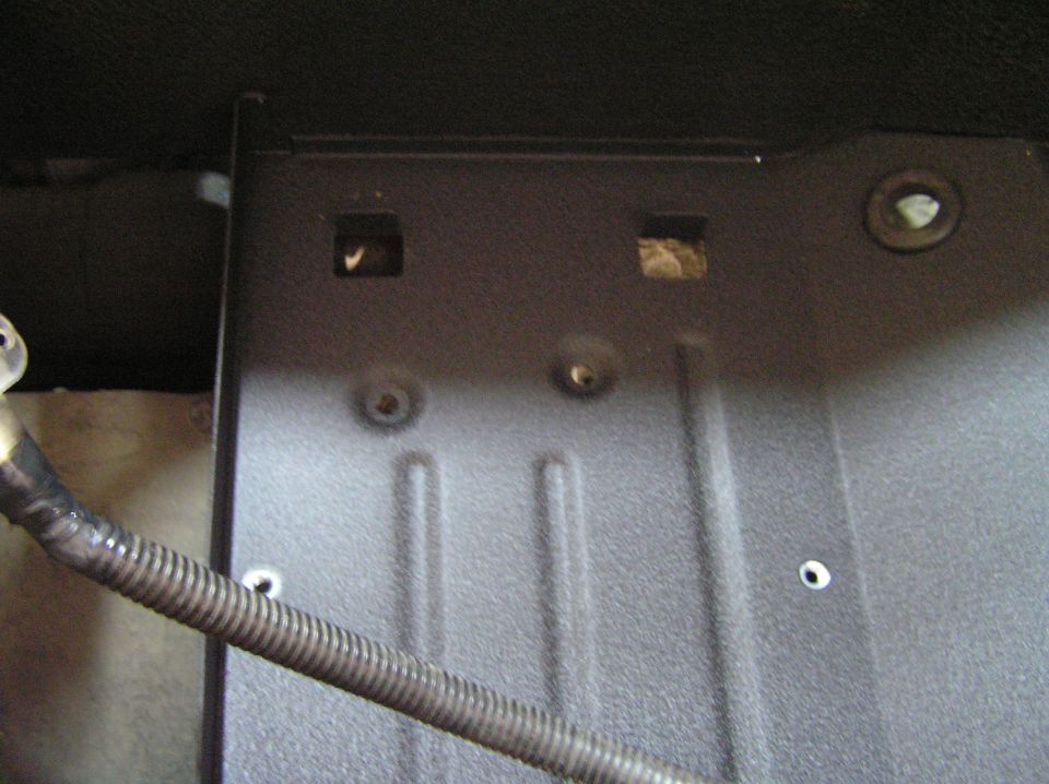 Dark metal floor pan panel with square holes, grommet and flex line