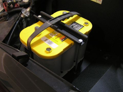 2000 Ford Excursion - Optima YellowTop battery secured with a black hold-down bracket in a vehicle's engine bay.