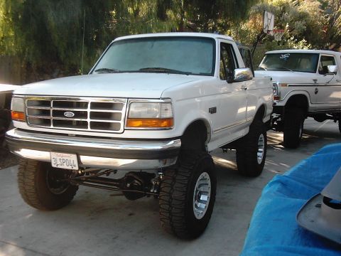 1978 Ford Bronco - Two lifted Ford trucks are parked in a driveway. The front truck is a white F-150.