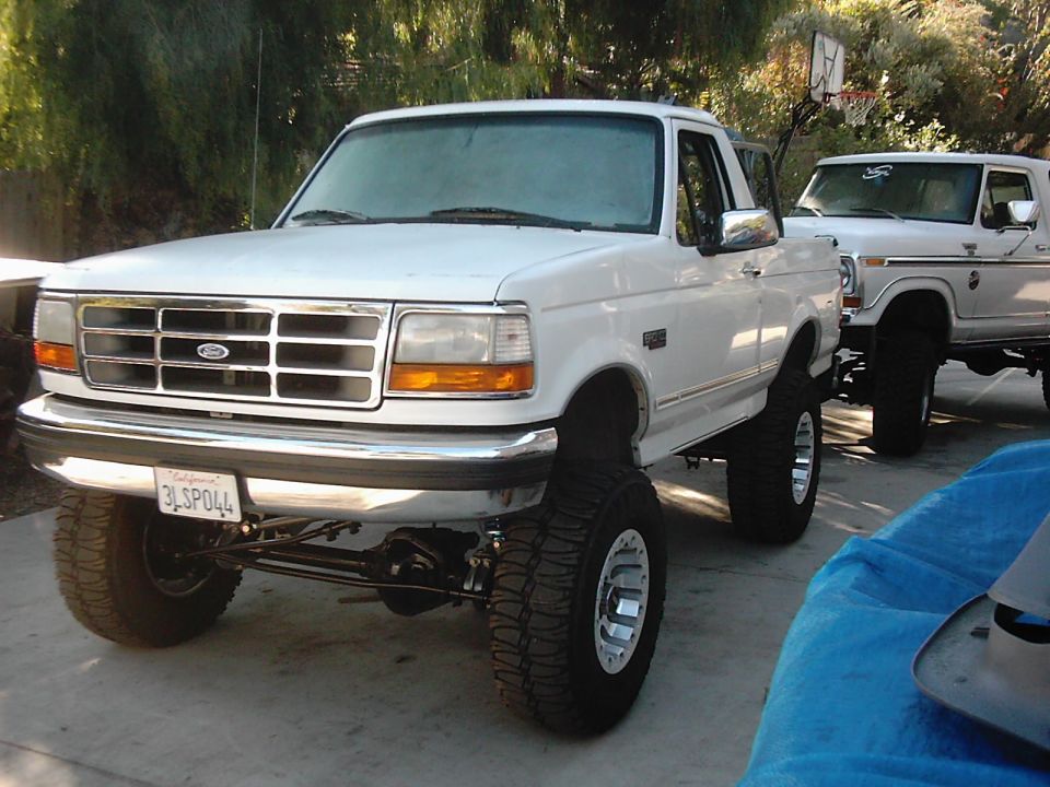 Lifted white Ford F-150 pickup and another Ford truck parked outside. License plate reads 3LSP044