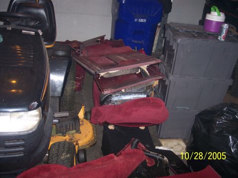 1994 Ford Bronco - Disassembled car interior parts are stored in a cluttered garage with lawnmowers and bins.