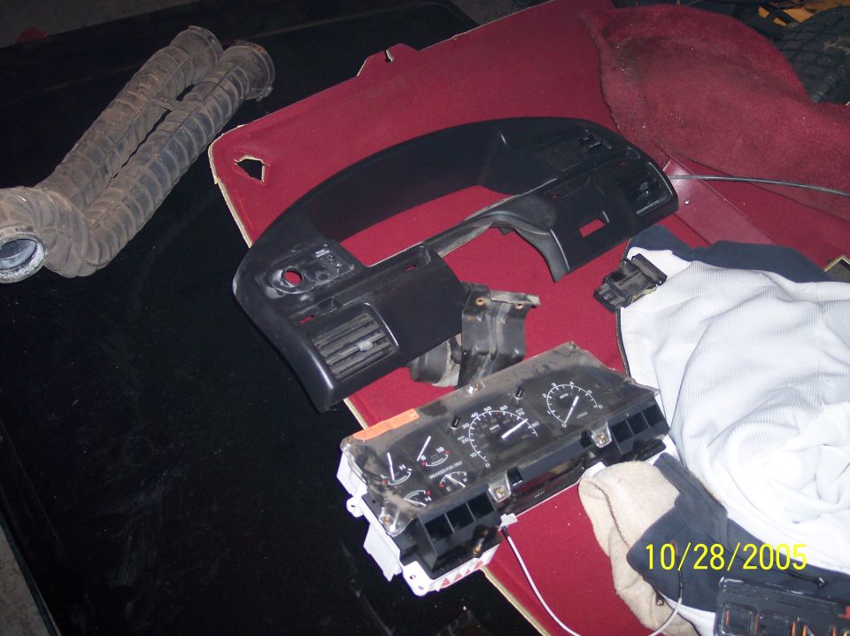 Dashboard trim, instrument cluster, and air intake hoses laid out on a red surface