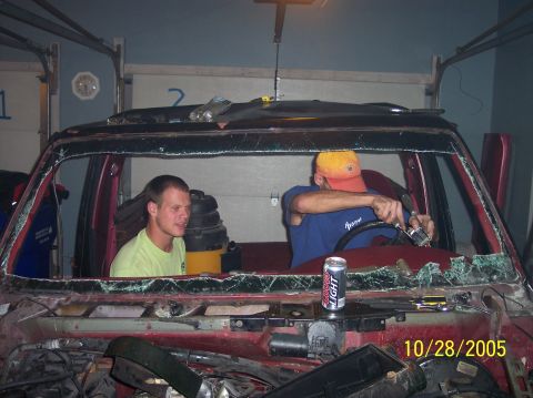 1994 Ford Bronco - Two men are inside a vehicle that appears to be undergoing repairs or a teardown, with a can of Coors Light on the dashboard.