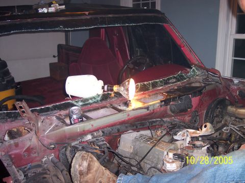 1994 Ford Bronco - The interior of a red SUV shows significant damage to the windshield and exposed engine components, with a work light illuminating the dash…