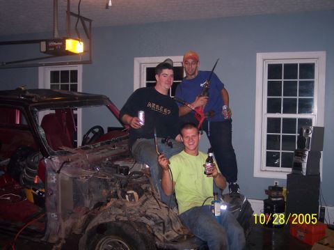 1994 Ford Bronco - Three men pose with tools and drinks next to a disassembled vehicle in a garage setting.