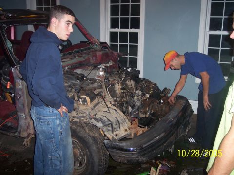 1994 Ford Bronco - A heavily damaged red SUV sits with its front end destroyed, as two men inspect the engine compartment.