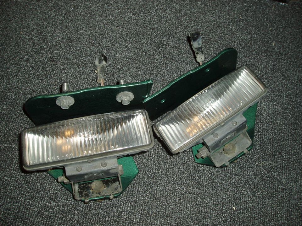 Two green headlight assemblies with clear lenses and metal brackets on a gray carpeted surface
